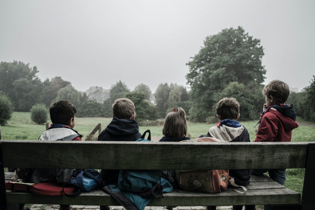 Fünf Kinder sitzen auf einer Bank, von hinten fotografiert